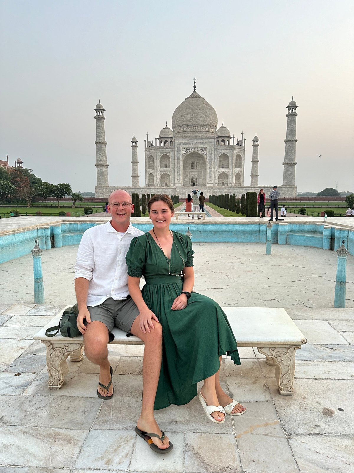 A couple sitting on a marble bench at the Taj Mahal with the iconic white dome and minarets in the background
